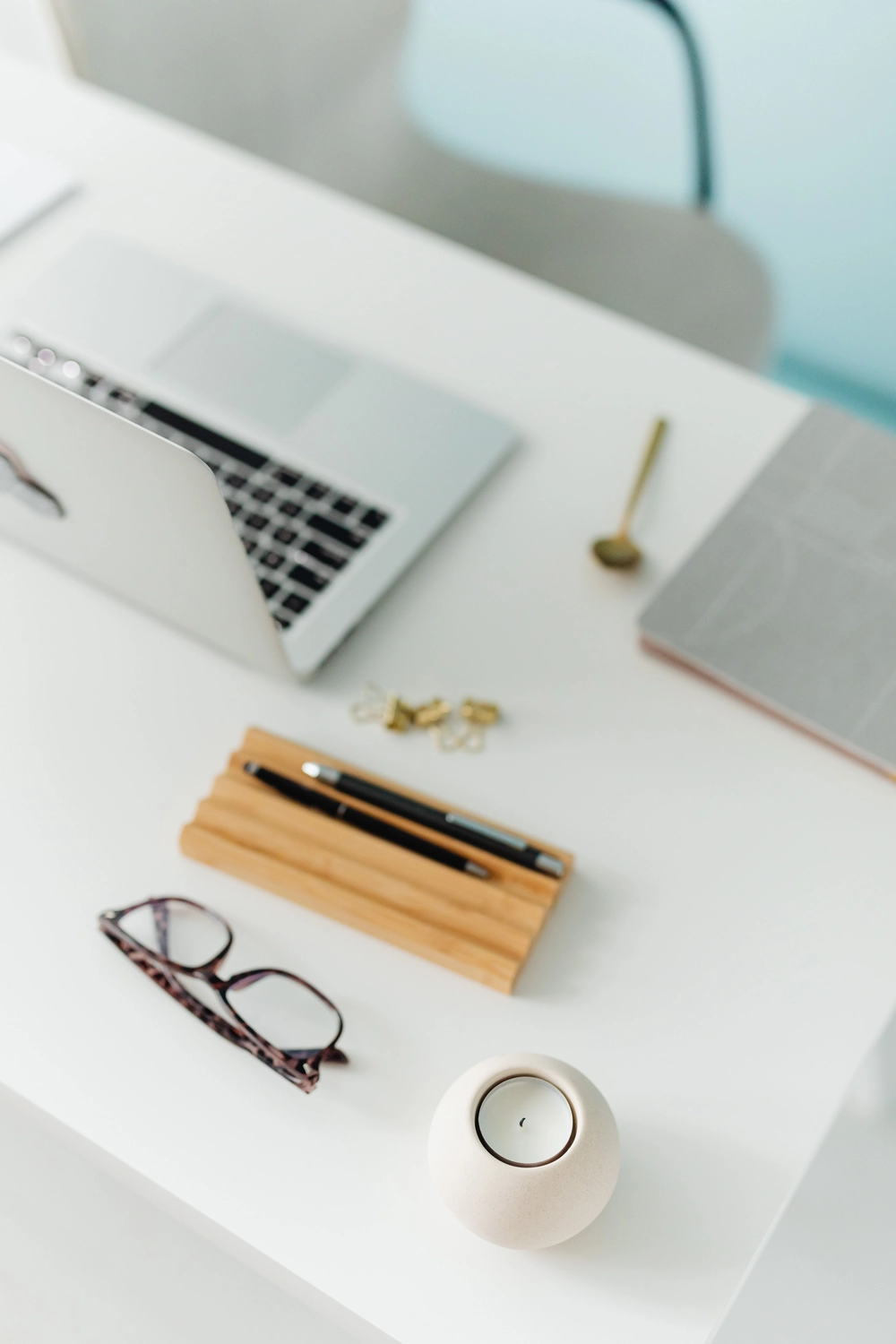 formelS GmbH – Berufsbildungszentrum Halle – Ein schlichter weißer Schreibtisch mit einem Laptop, einer Brille, Stiften in einem Holzständer und einer kleinen Kerze.