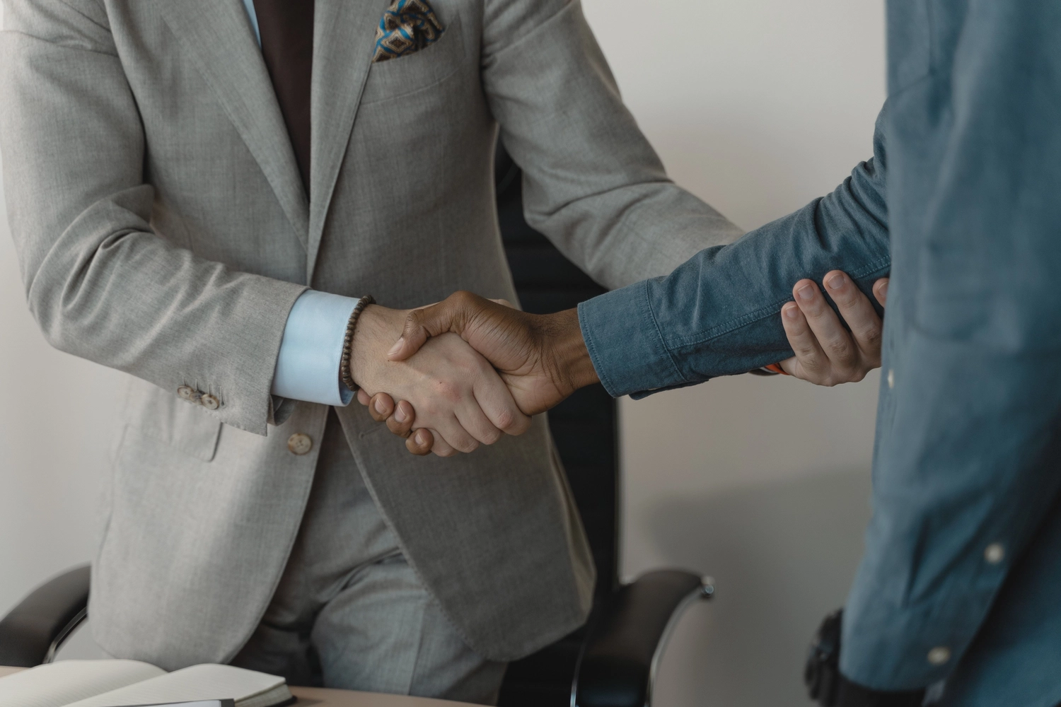 formelS GmbH – Berufsbildungszentrum Halle – Zwei Personen geben sich die Hand: Die eine trägt einen grauen Anzug, die andere ein Jeanshemd; die Szene spielt in einem Büro.